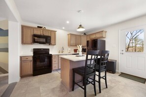 A modern kitchen with wooden cabinets, a central island with chairs, a black refrigerator, and a microwave.