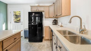 Eine Küche mit Holzschränken, einem schwarzen Kühlschrank, einer Edelstahl-Spüle und einer Kaffeemaschine.