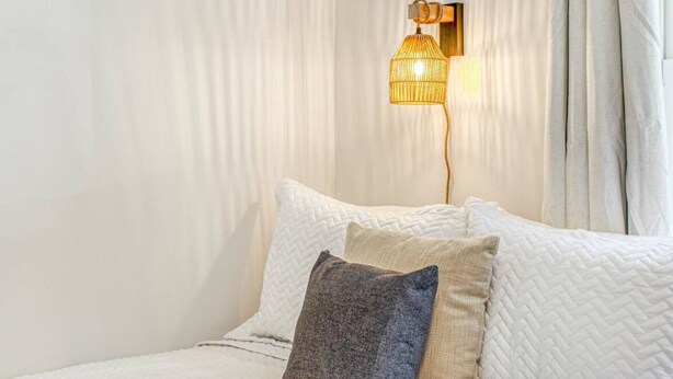 Ein Bett mit weißer Steppdecke, zwei Kissen und einer gemusterten Tagesdecke.