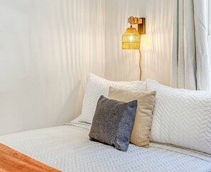 Un lit recouvert d’une couette blanche matelassée, avec deux oreillers et un plaid à motifs.