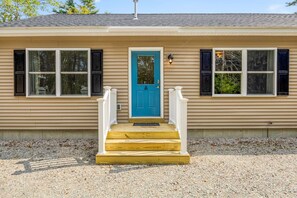 A single-story house with a blue front door, white railings, and a gravel driveway.