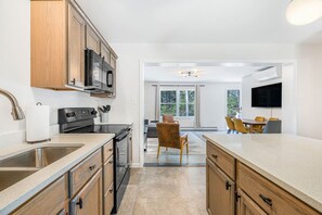 A modern kitchen with wooden cabinets, a stainless steel sink, and a built-in microwave. - Maine Forest Hideaway (Ellsworth)