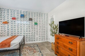 A bedroom with a bed, a dresser, a television, and a wall with leaf-patterned wallpaper.