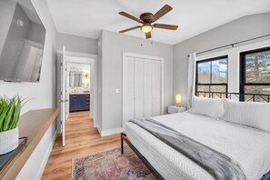 A bedroom with a bed, a ceiling fan, a nightstand, a window, and a view of the outdoors.
