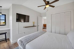 Une chambre à coucher comprenant un lit, un ventilateur de plafond, une télévision, une fenêtre avec vue et une armoire.