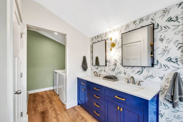 A bathroom with a double vanity, a mirror, a towel rack, and a radiator.