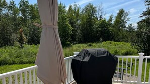 Una terrassa de fusta amb una taula rodona i cadires, un parasol i una barbacoa.