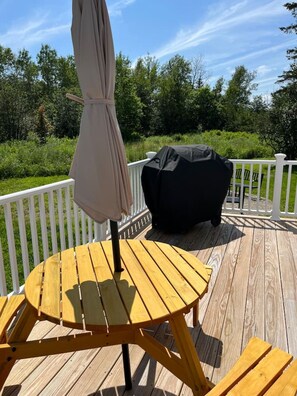 Un terrazza in legno con un tavolo rotondo e sedie, un ombrellone e un barbecue.