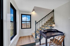 A staircase with a wooden handrail and a black railing, leading to a landing with a table and a chair.