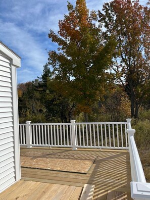 Une terrasse en bois avec une balustrade blanche, entourée d’arbres aux feuilles d’automne.