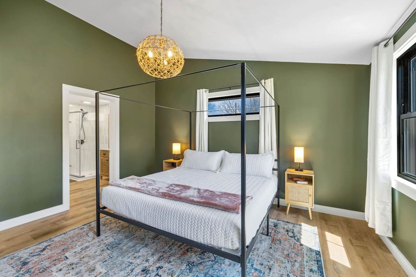 A four-poster bed with a canopy, bedside tables with lamps, a patterned rug, and a view of the outdoors.
