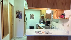 A compact kitchen with wooden cabinets, a white countertop, and a clock on the wall. - Charming 1-bedroom house with big yard, AC and WiFi in delightful Fort Mohave (Fort Mohave)