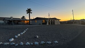 A building with a parking area, a palm tree, and a clear sky. - Charming 1-bedroom house with big yard, AC and WiFi in delightful Fort Mohave (Fort Mohave)