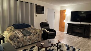 A living room with a sofa, armchair, coffee table, and a flat-screen TV. - Charming 1-bedroom house with big yard, AC and WiFi in delightful Fort Mohave (Fort Mohave)