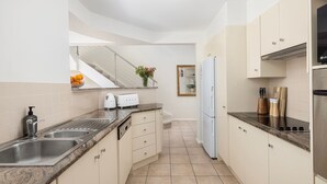 A modern kitchen with a granite countertop, stainless steel appliances, and beige cabinetry. - Swell – walk to Fingal Bay Beach, swimming pool, outdoor BBQ entertaining (Fingal Bay)