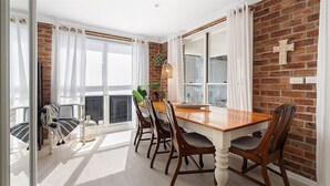 Een eetruimte met een bakstenen muur, witte gordijnen en een houten tafel met stoelen.
