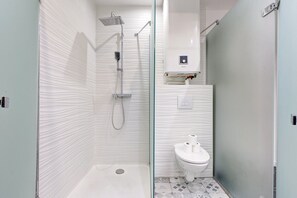 Een moderne badkamer met een douchecabine van glas, een toilet en een klein plankje met toiletartikelen.