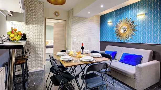 Un comedor moderno con una mesa dispuesta para cuatro personas, un sofá con cojines azules y una pared decorativa con un diseño de sol.