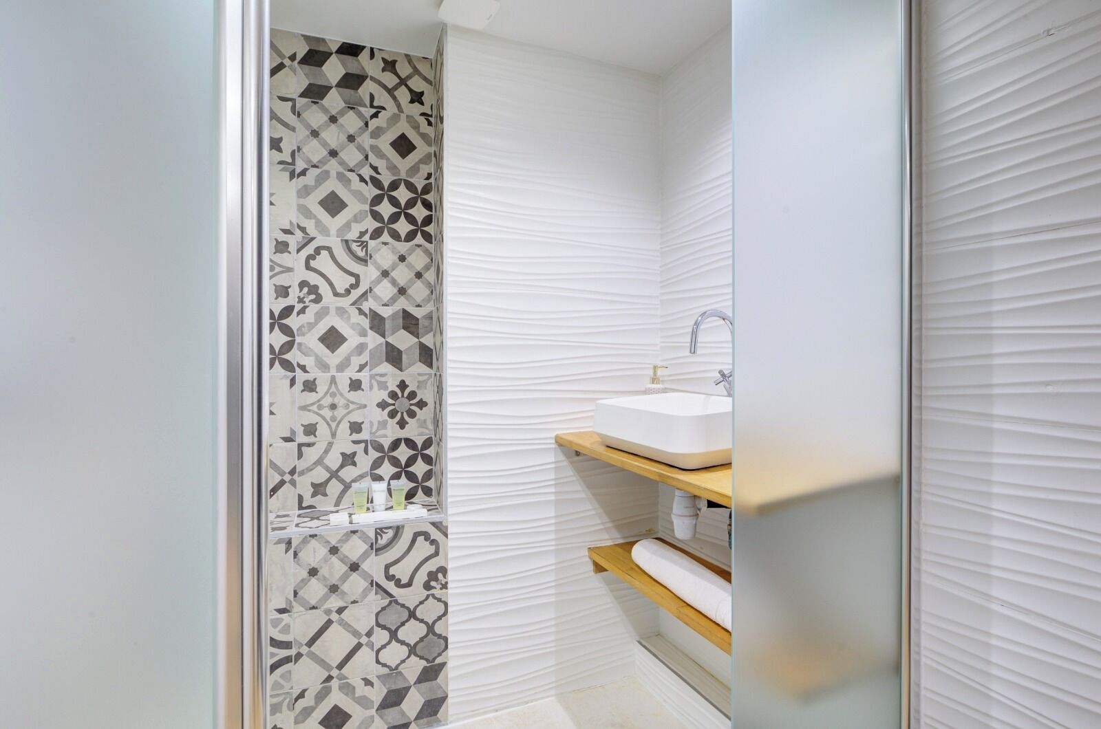 A bathroom with a patterned tile wall, a white sink, and a wooden shelf.