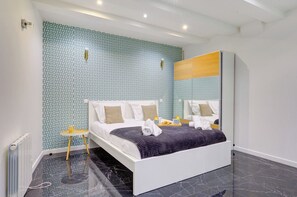 A modern bedroom with a patterned wall, a bed with white bedding, a bedside table, and a mirror.