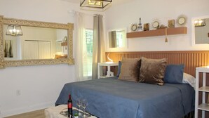A bedroom with a bed, bedside tables, a mirror, and a shelf with decorative items.
