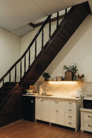 A kitchen with a wooden staircase, white cabinets, and a tiled backsplash.