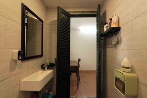 A narrow bathroom with a sink, mirror, and open door leading to a hallway.