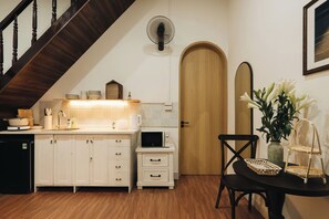 Cocina con escalera de madera, microondas, lavabo y comedor con una silla y mesa.