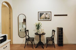 A room with a wooden door, a round mirror, a framed picture of a bicycle, a small round table with chairs, a shoe rack, and a white cabinet with a microwave. - Dusk House - 3BR house with city view (Hanoi)