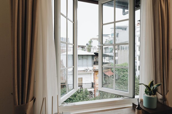 Una habitación con un ventanal, cortinas, una mesita con una planta y un alféizar con una botella.