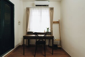 A room with a wooden desk, a chair, a potted plant, and a window with curtains.