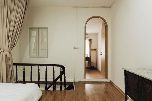 A bedroom with a wooden bed, a window with curtains, and a hallway leading to another room.