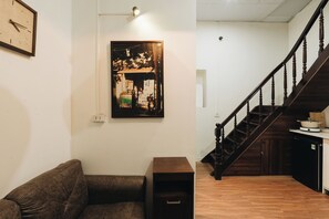 A room with a wooden staircase, a sofa, a framed picture on the wall, and a small cabinet.