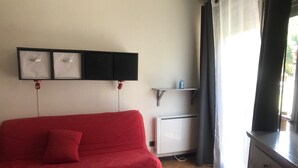 A red sofa with a cushion, a white cabinet, and a shelf with a bottle. - Studio in the mountains, 8 minutes from the slopes (Saint-Lary-Soulan)