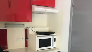 A compact kitchenette with red cabinets, a white microwave, and a small dishwasher. - Studio in the mountains, 8 minutes from the slopes (Saint-Lary-Soulan)