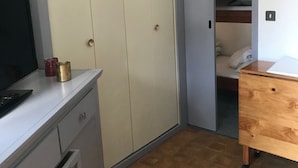 A small, compact room with a wardrobe, a desk with a computer and two cups, a wooden dresser, and a bed in the corner. - Studio in the mountains, 8 minutes from the slopes (Saint-Lary-Soulan)