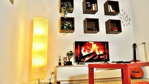 A living room with a flat-screen TV, wooden shelves with books and plants, a guitar, and a table with a remote control. - Close Cinecittà studios suitable for families and pets Metro 5 minutes walking (Roma)