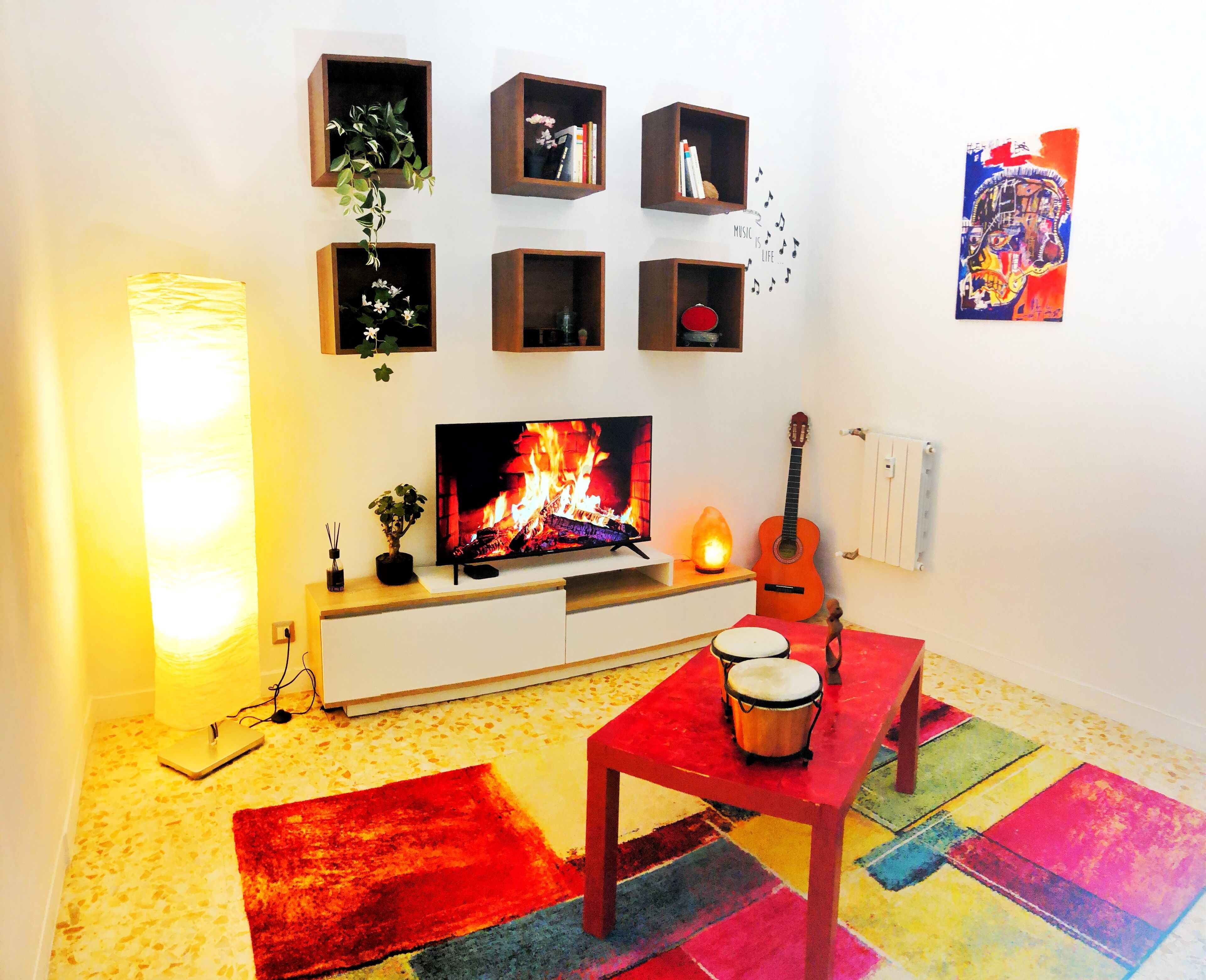 Uma sala de estar com televisão, lareira, guitarra e bateria.