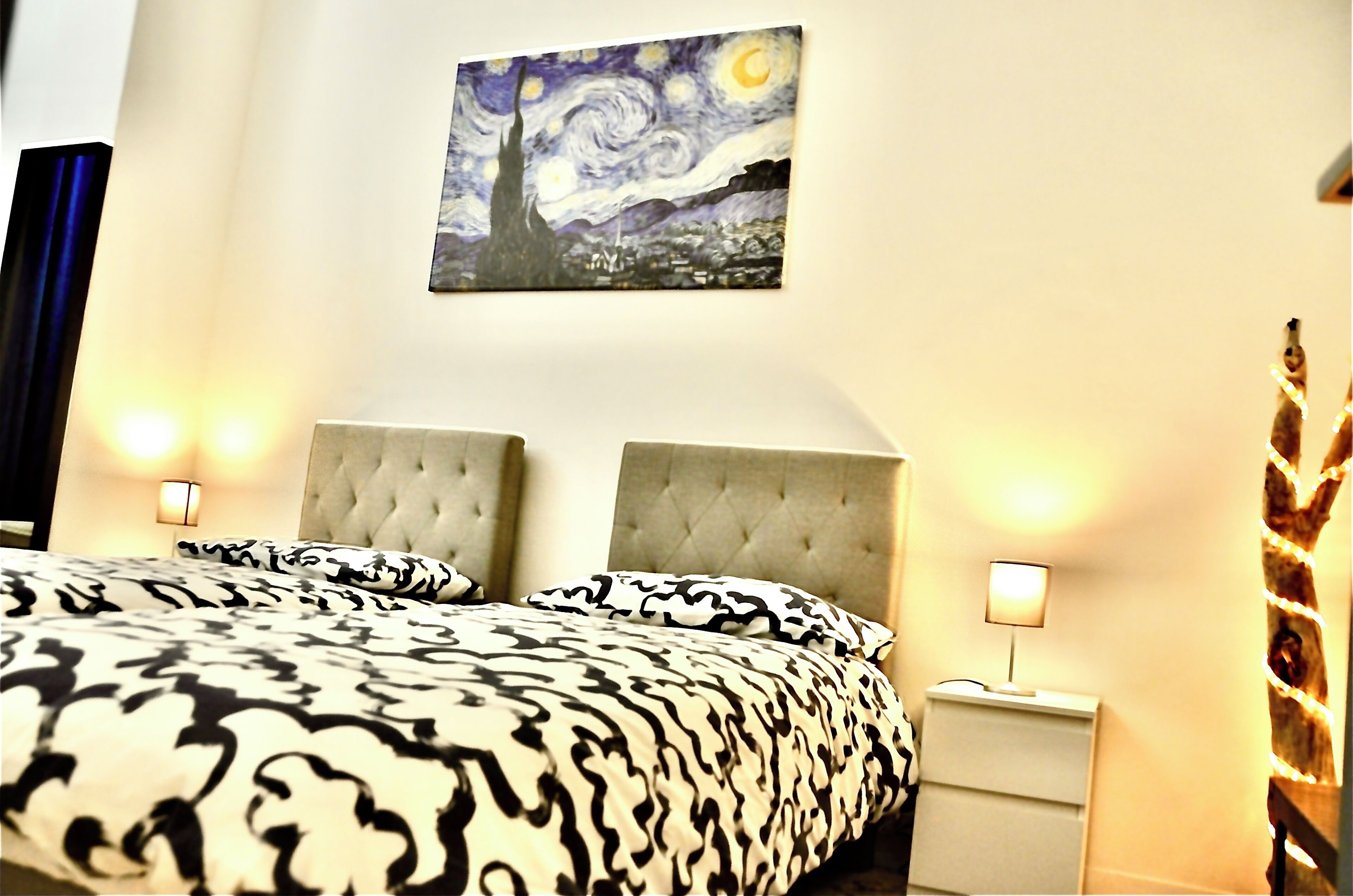 A bedroom with a tufted headboard, a bed with patterned bedding, a wall-mounted painting, and bedside lamps.