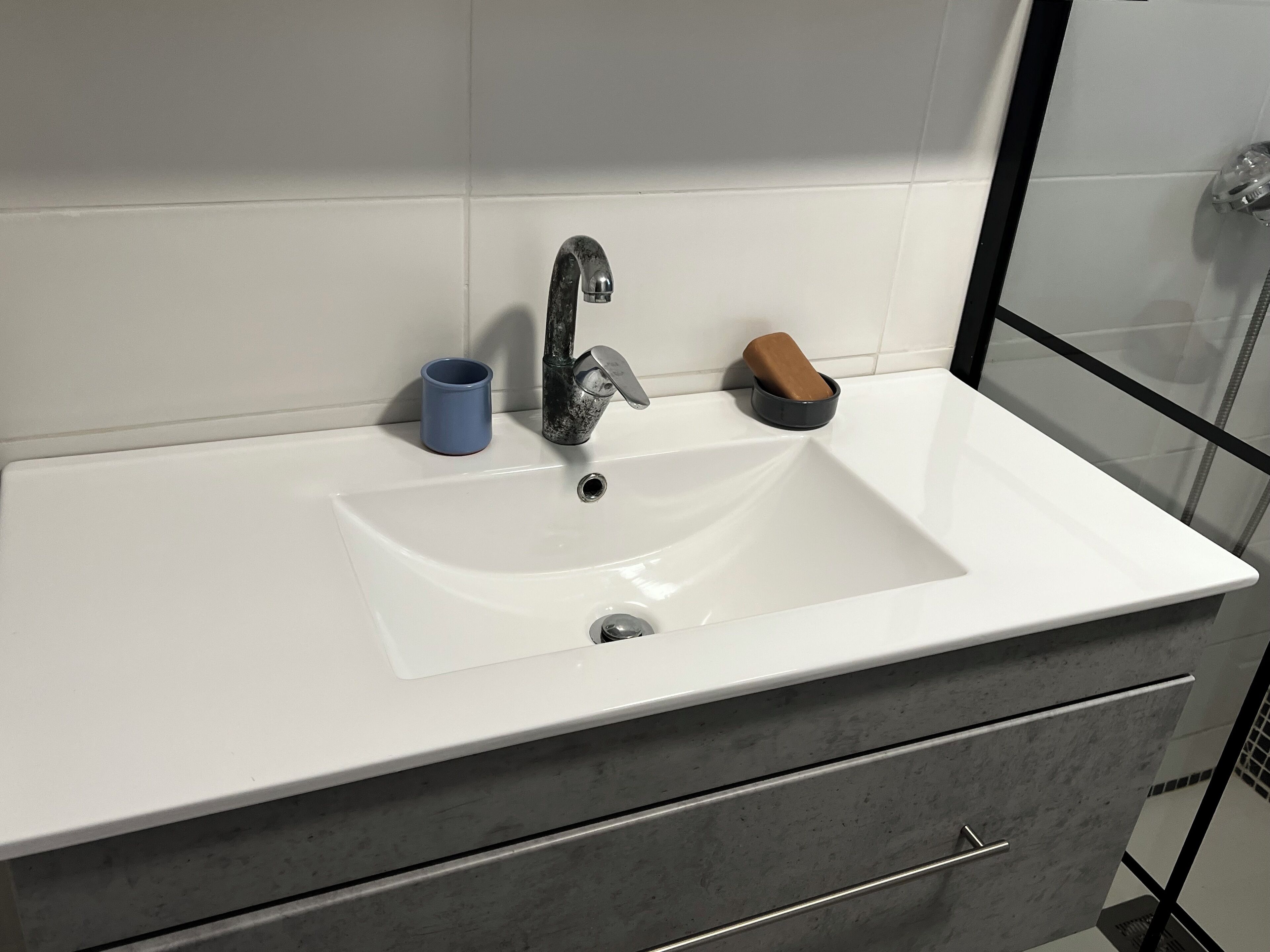 A bathroom with a white sink, a blue cup, and a soap dish.