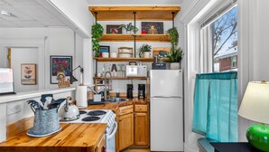 Cocina compacta con armarios de madera, un refrigerador blanco y una ventana con cortina azul aguamarina.