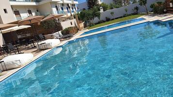 A clear blue pool with a tiled edge, surrounded by lounge chairs and umbrellas.