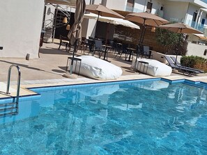 A swimming pool with lounge chairs and umbrellas, surrounded by a building with a tiled exterior. - SOHO BLUE city hotel (Hersonissos)