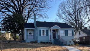 A single-story house with a front porch, a chimney, and a small front yard.