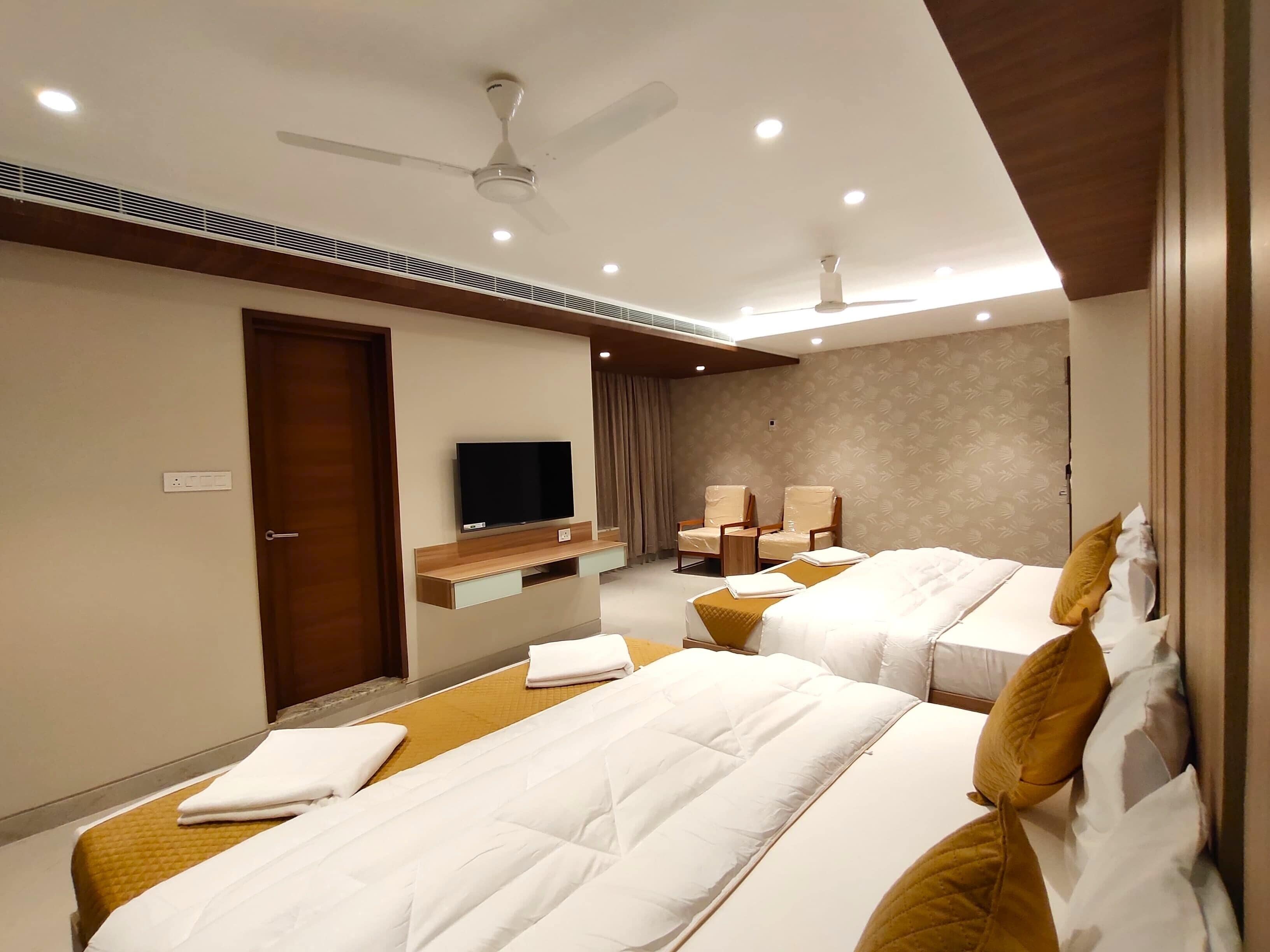 Habitación de hotel con dos camas, televisión, ventiladores de techo y una pequeña zona de estar.