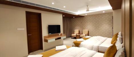 Habitación de hotel con dos camas, televisión, ventiladores de techo y una pequeña zona de estar.