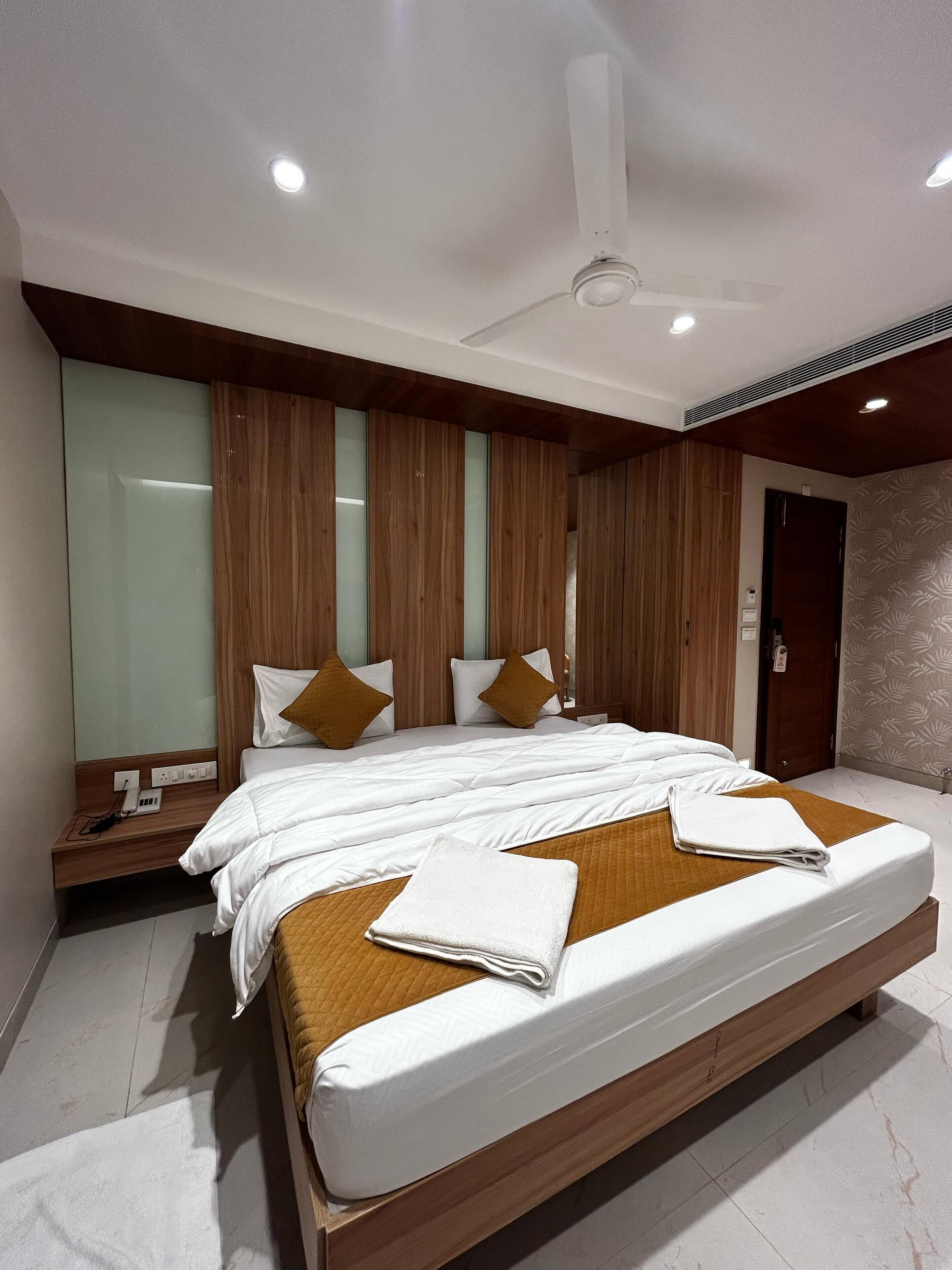 A modern hotel room with a large bed, wooden paneling, a ceiling fan, and a nightstand with a phone.