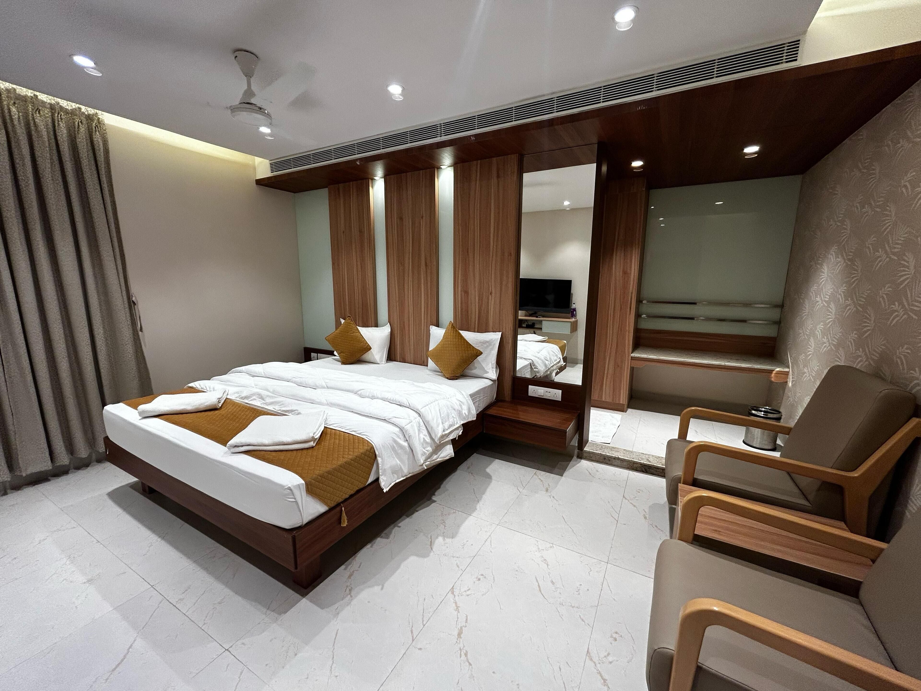 A modern hotel room with a large bed, a seating area with a chair, a television, and a window.