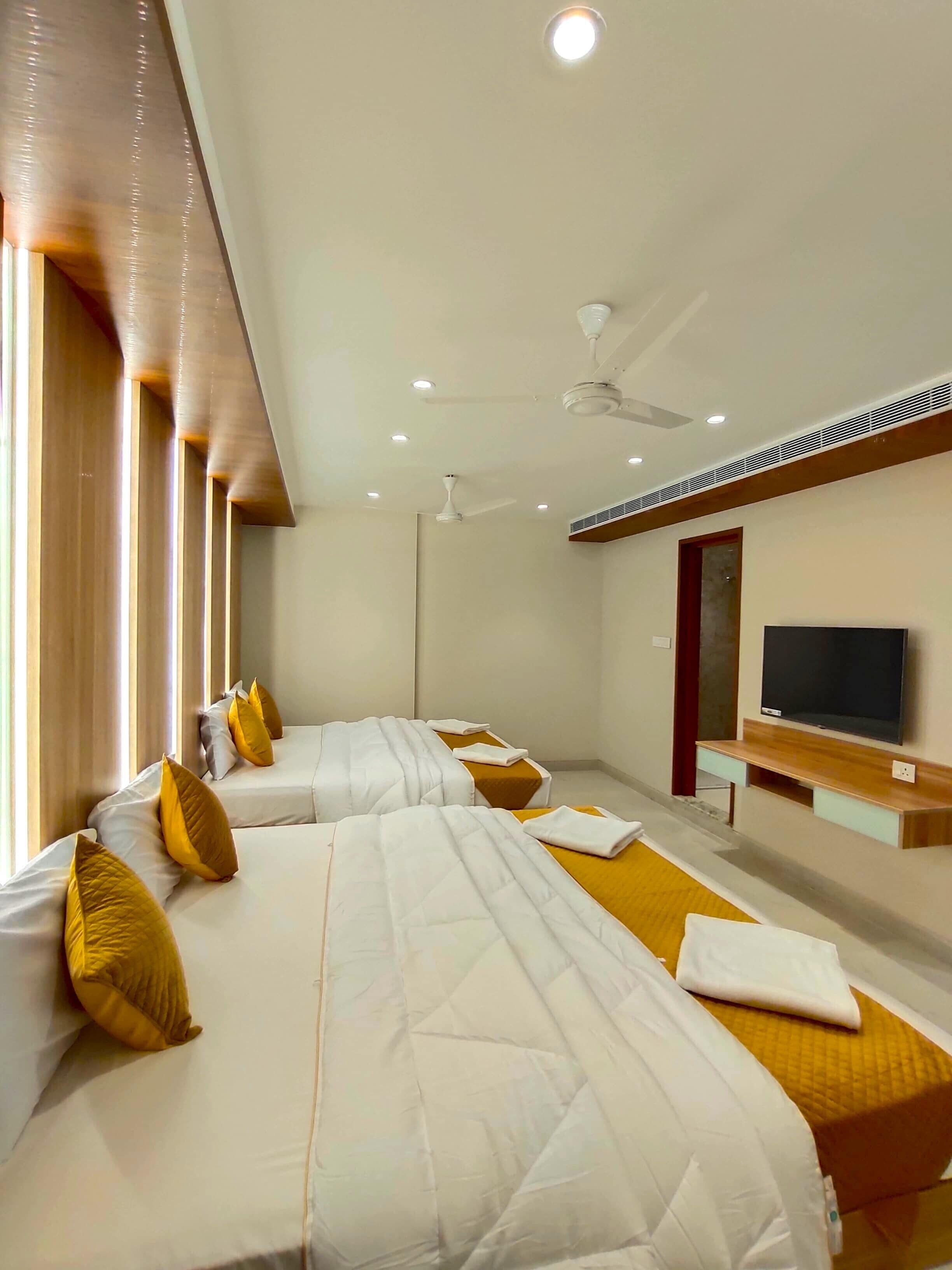 A hotel room with two beds, a TV, and a ceiling fan.