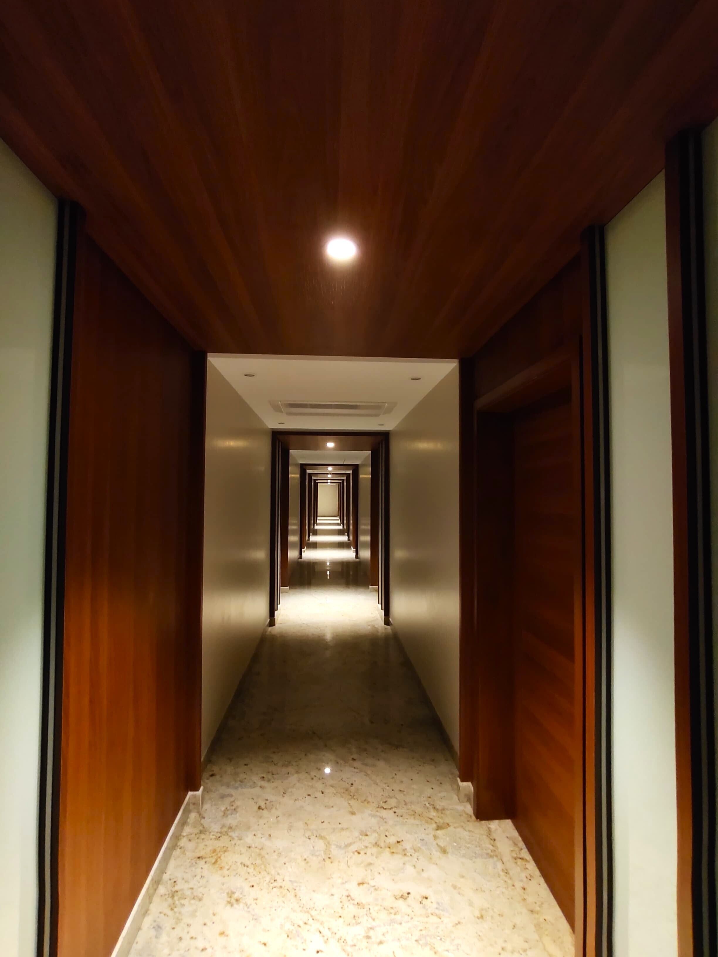 A long, narrow hallway with wooden paneling on the walls and a marble floor.